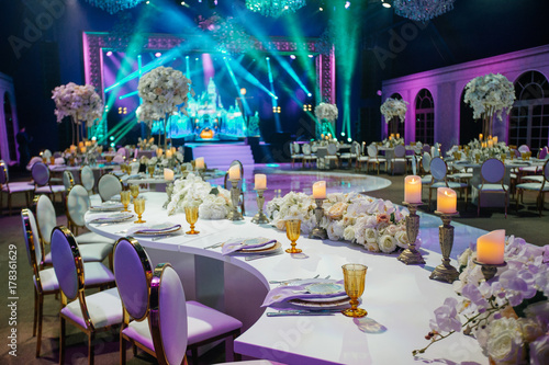Long dinner table decorated with white flowers, shiny candles and golden glasses stands in a beautiful hall photo