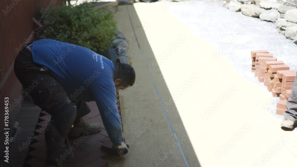 Laborer catches red bricks and puts them down into a herringbone patter on a hardscaping project. Laborer catches red bricks and puts them down into a herringbone patter on a hardscaping project.