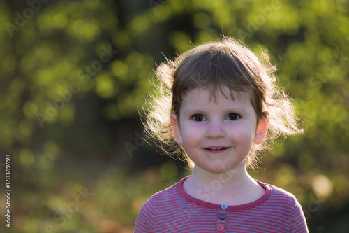 Portret małej dziewczynki w plenerze. Rozmyte tło jesiennych drzew.