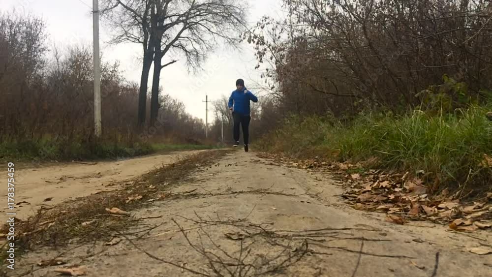Low angle Road runner man running in autumn park. Slow motion shot of young man jogging in the park. Low angle Road runner man running in autumn park. Slow motion shot of young man jogging in the park.