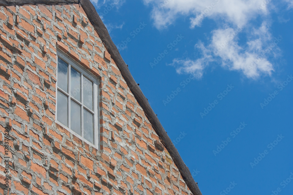 Window on brown brick wall and wooden roof in vintage style with blue sky background.