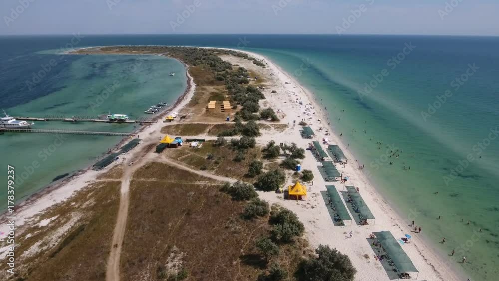 An impressive bird`s eye view of a narrow sand spit of Dzharylhach island in the Black Sea. The island is covered with sunshades on its sandy coast in summer. The pier with a ship is seen too. An impressive bird`s eye view of a narrow sand spit of Dzharylhach island in the Black Sea. The island is covered with sunshades on its sandy coast in summer. The pier with a ship is seen too.