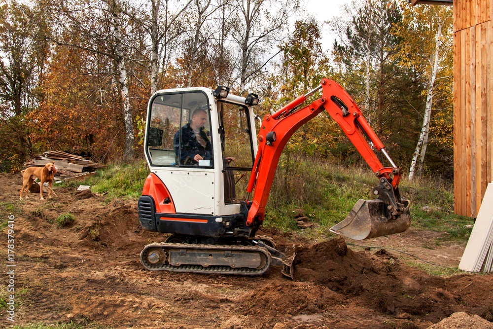 Mini excavator on construction site. Excavator regulates the terrain around the house. Mini excavator on construction site. Excavator regulates the terrain around the house.