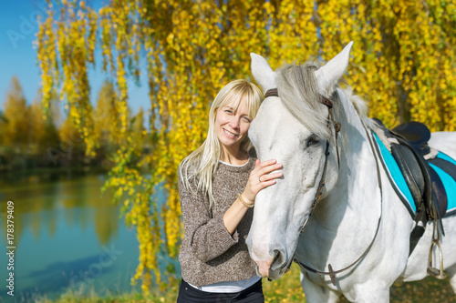 Beautiful and natural young woman spending sometime with her white horse.