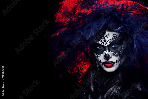 Close up studio portrait of beautiful woman with Halloween sugar skull makeup in red and black colors, wearing bridal veil. Model looking at camera. Dark, dead bride. Copy, empty space for text. 