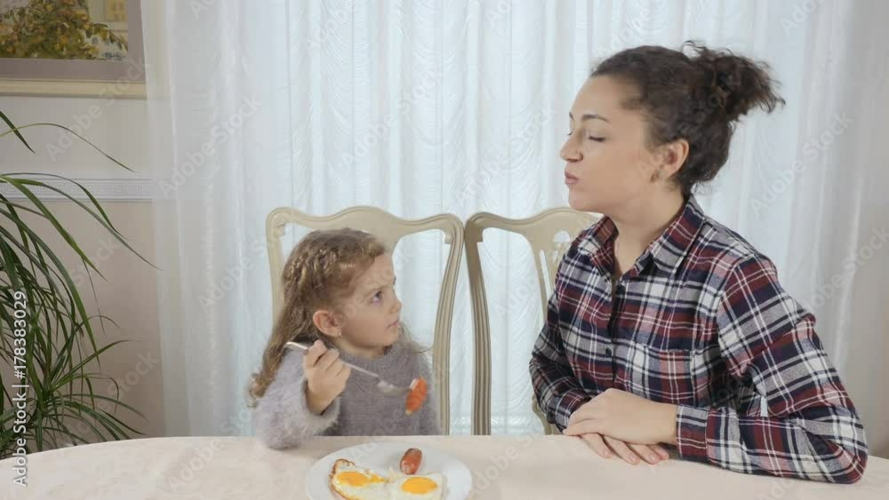 Little girl feeds her mother with sausage Little girl feeds her mother with sausage