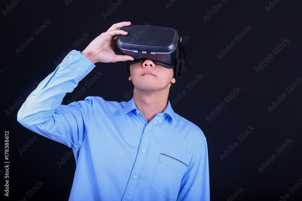 Young Asian man wearing virtual reality goggles with black background studio. Smartphone using with VR headset. Young Asian man wearing virtual reality goggles with black background studio. Smartphone using with VR headset.