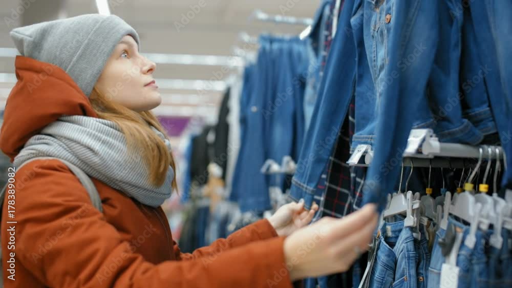 Young Lady is Choosing Jean Denim Jacket in the Big Shop with Clothes Young Lady is Choosing Jean Denim Jacket in the Big Shop with Clothes