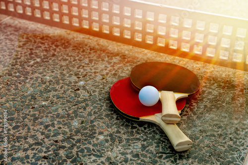 Close up of ping-pong ball with tennis rackets on stone tennis table in sunny lights, Equipment for outdoors table tennis. Outdoor sport concept.healthy lifestyle and objects concept