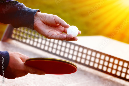 Close up of tennis player hands with tennis racket on nature background in sunny day.Closeup shot of a man serving in table tennis. Outdoor tennis table play