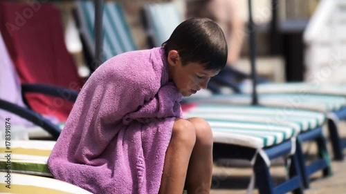 boy in a towel warms on a lounger after swam in the swimming pool