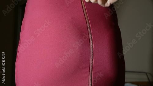 Female fingers unfasten the zipper on a red skirt. visible panties