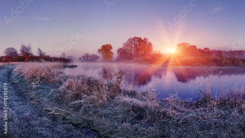 Sunrise on autumn frosty nature. Landscape of bright dawn over river. grass with hoarfrost shining on sun lights