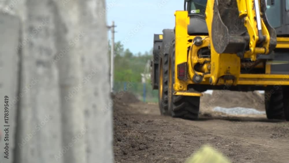 Refocus from concrete slabs on a yellow construction tractor that rides on a dirt road Refocus from concrete slabs on a yellow construction tractor that rides on a dirt road