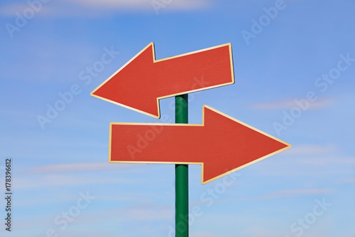 Road sign with two red arrows over blue sky
