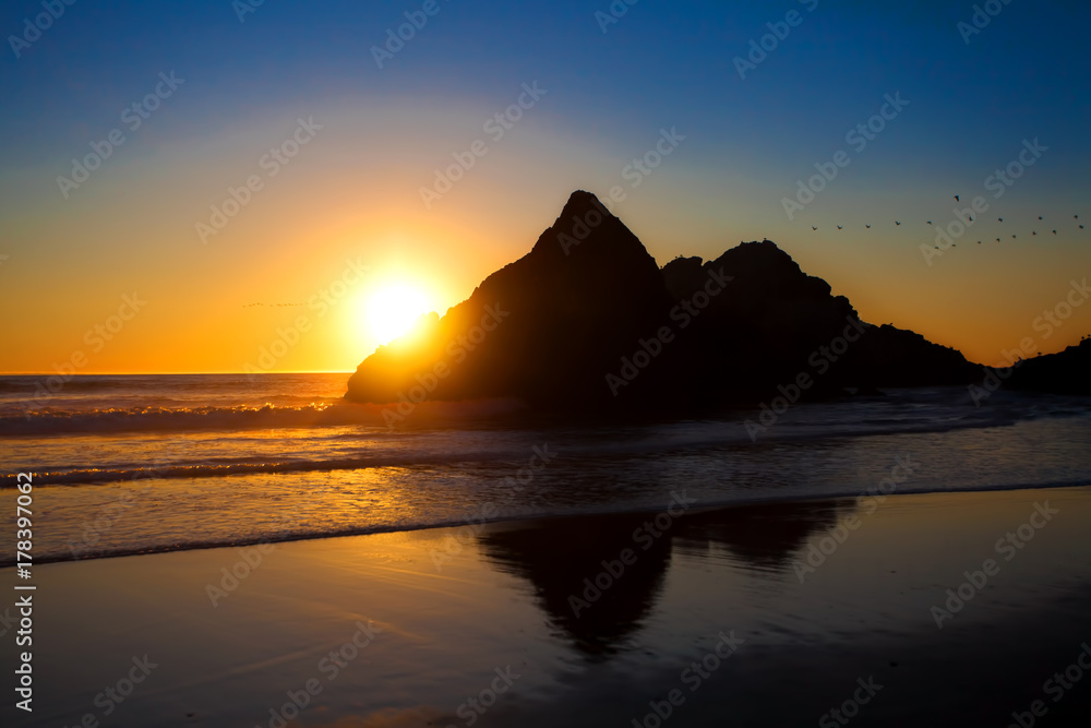 Soft beautiful sunset behind large rock along Pacific Ocean beach