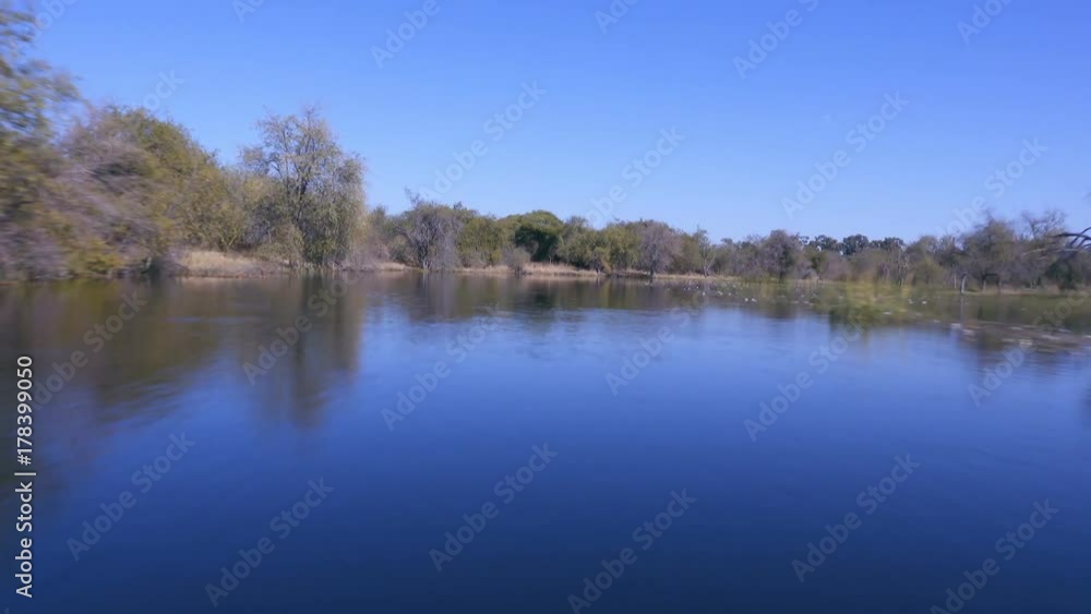 Speeding down rural river with acacia scrub trees on either side Speeding down rural river with acacia scrub trees on either side