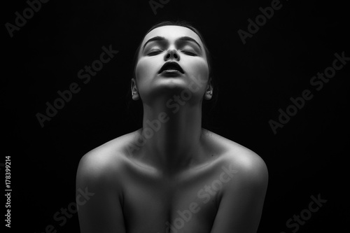 beautiful young naked woman posing sensually holding head up on black background, monochrome