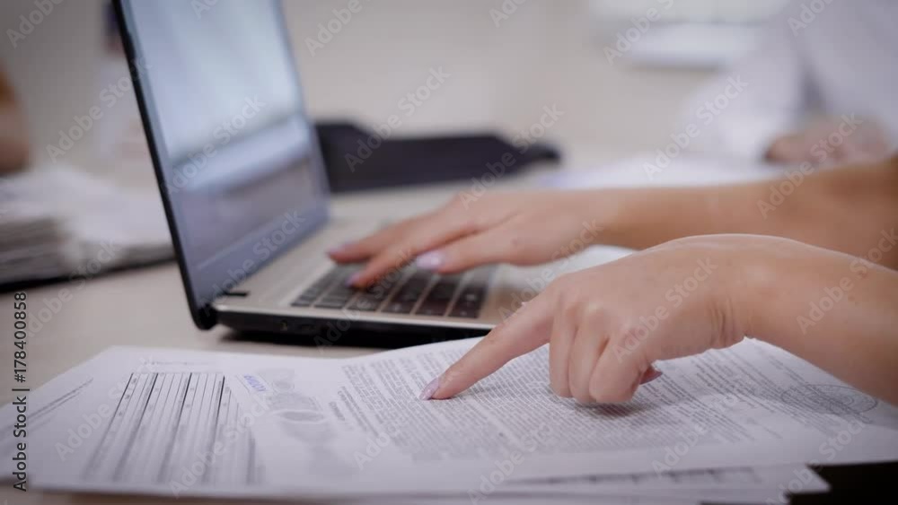 Crop woman typing on laptop and reading carefully important paper