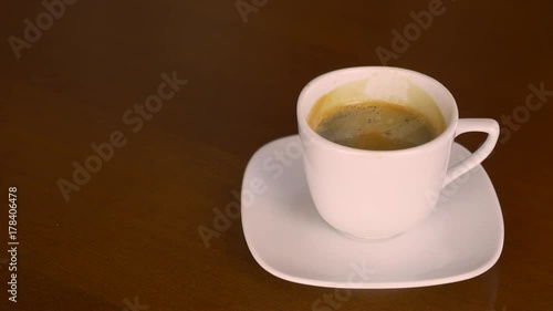 Close up white cup of freshblack coffee espresso. Hand take coffee drink and put back on plate. Wooden table derk brown color. Coffee drinking concept for coffee lovers caf restorante barista. photo