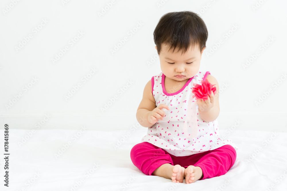 Portrait of adorable baby sitting on a white floor and holding head band Portrait of adorable baby sitting on a white floor and holding head band