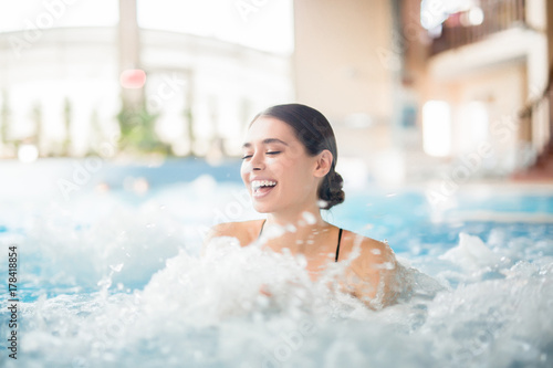 Excited female laughing while splashing warm water during spa procedure in whirlpool photo