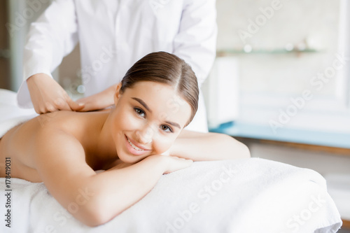 Happy girl enjoying massage of her back in dayspa salon