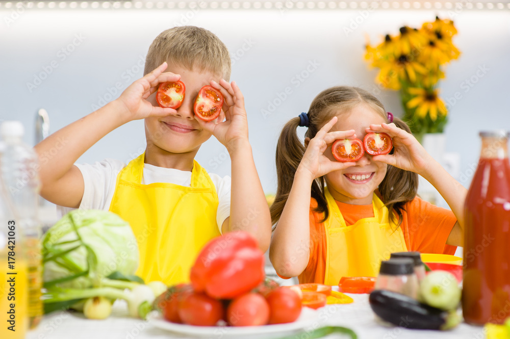 Happy kids having fun with food vegetables at kitchen holds tomatoes before his eyes like in glasses Happy kids having fun with food vegetables at kitchen holds tomatoes before his eyes like in glasses