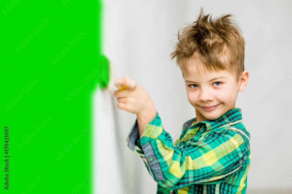 Young boy painting the wall with paintbrush in green. Space for text Young boy painting the wall with paintbrush in green. Space for text