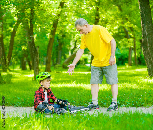 Father helps to rise to the son who has fallen down rolling on roller skates