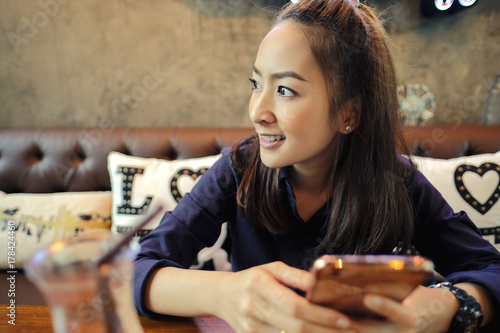 Young charming woman holding with telephone while sitting alone in coffee shop during free time, attractive female with cute smile having sit relaxing with mobile phone while rest in cafe
