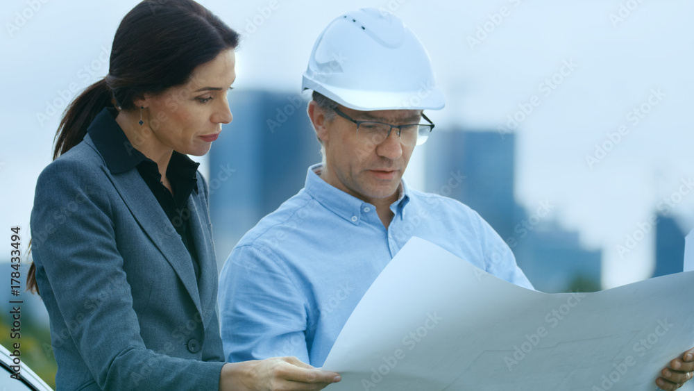 Chief Engineer Shows Project Drafts To Business Woman Investor. In the Background City with Skyscrapers. Chief Engineer Shows Project Drafts To Business Woman Investor. In the Background City with Skyscrapers.