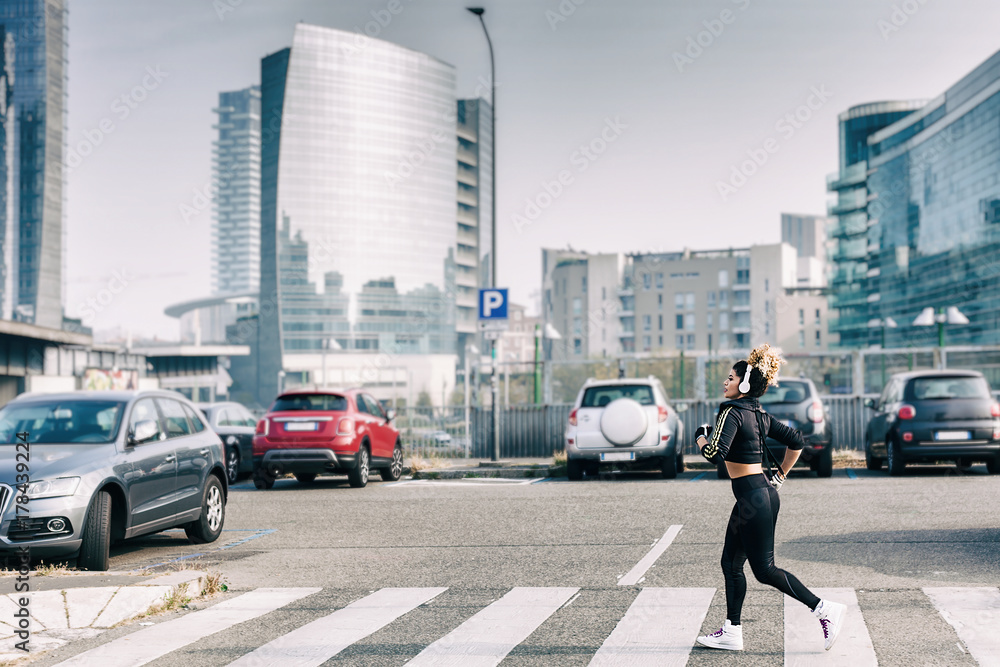 Beautiful jogger portrait running on pedestrian crossing near urban parking lot