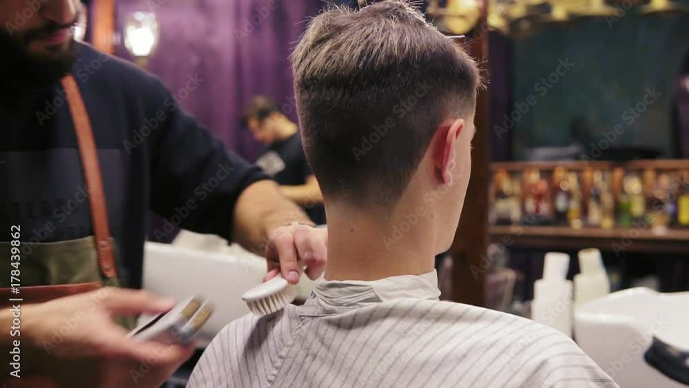 Back view of a client getting his hair cut by a barber. The bearded hairdresser is cutting hair using electric trimmer Back view of a client getting his hair cut by a barber. The bearded hairdresser is cutting hair using electric trimmer