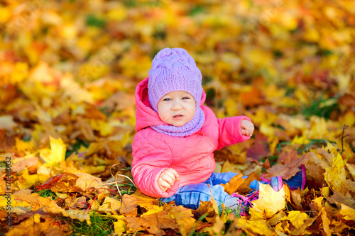 beautiful baby in autumn park  sits on foliage and looks at camera.