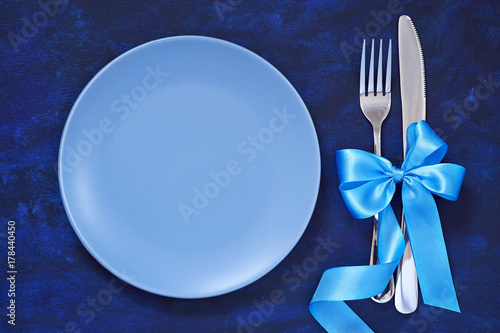 Festive table setting with Christmas ornaments Christmas tree branches, toys and a blue satin bow and ribbon, Plate and Cutlery