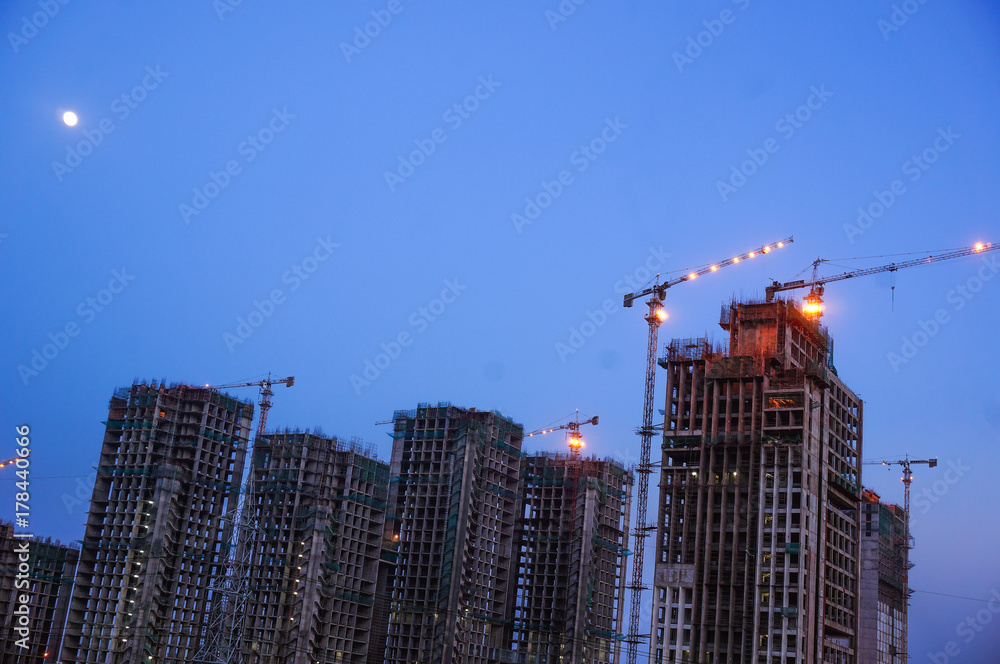 Fototapeta premium Under construction building with cranes, supports and other construction equipment. Shot against the twilight sky in a major city like Gurgaon, Delhi, Noida, Hyderabad.