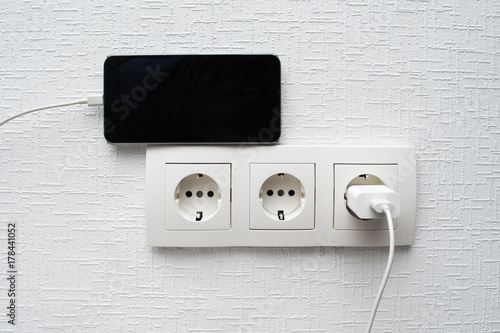 European set of sockets on the wall with mobile phone charging photo