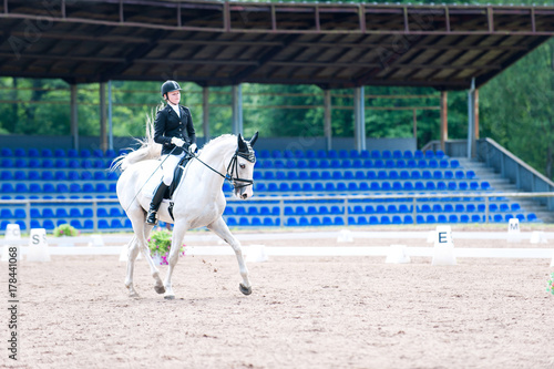 Teenage girl equestrian in dress uniform riding horseback on arena