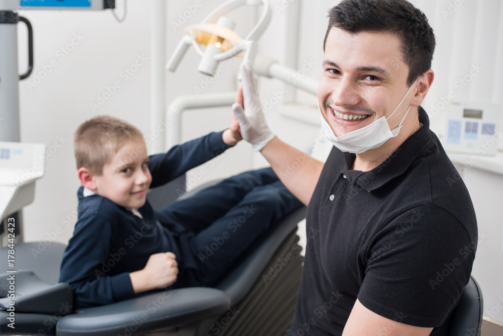 Pediatric dentist shake hands with young boy, congratulate patient for