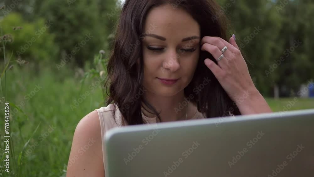 Beautiful woman sits on a park bench with a laptop typing on the keyboard Beautiful woman sits on a park bench with a laptop typing on the keyboard