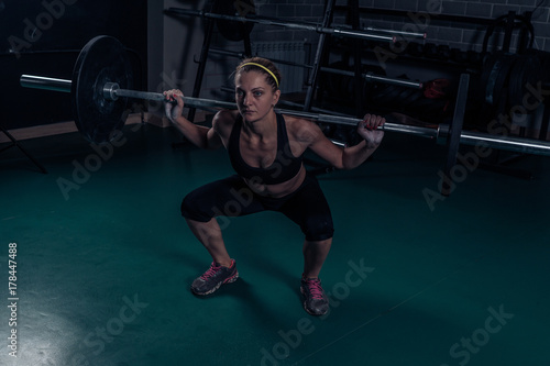 Crossfit Muscular strong woman crouching with heavy weight in the gym