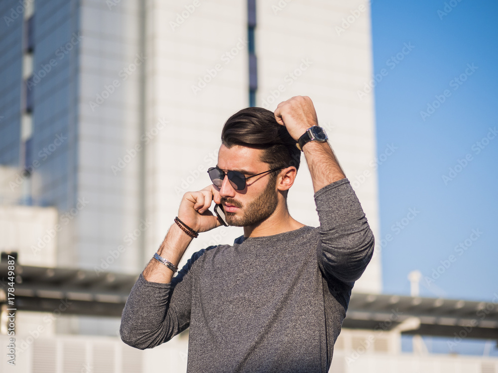 Handsome man making a phone call, talking on cell phone, standing outdoor during daytime in business district Handsome man making a phone call, talking on cell phone, standing outdoor during daytime in business district