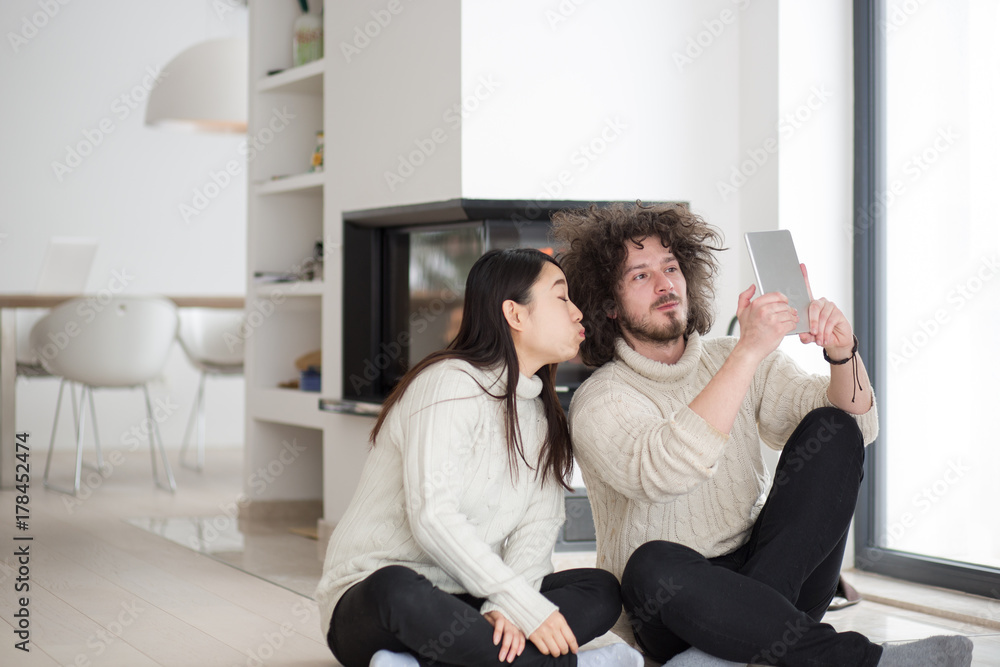 multiethnic couple using tablet computer in front of fireplace multiethnic couple using tablet computer in front of fireplace