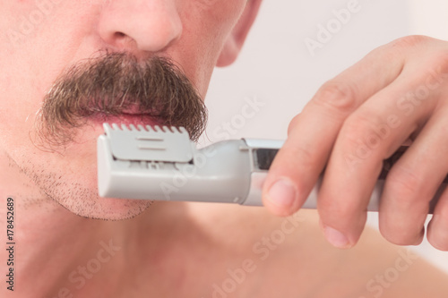 An unshaven man is cutting his mustache with a trimmer. Close-up. photo