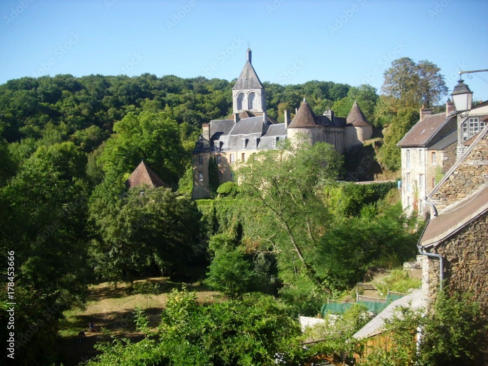 Château de Gargilesse entouré d'arbres. Détail du  village au premier plan sur la droite. Colline boisée et ciel bleu  en arrière-plan. 