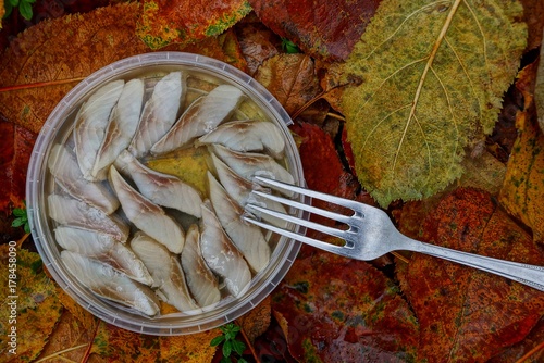 тарелка с кусками сельди в масле и вилка на жёлтых листьях