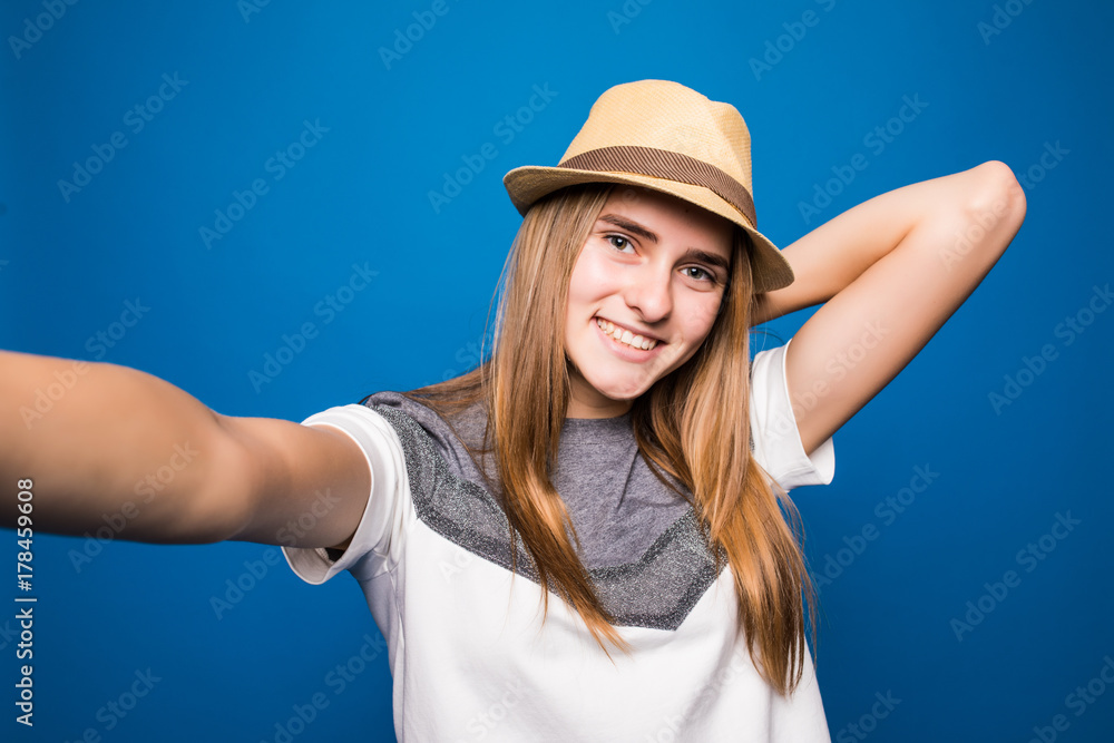 Trendy beautiful hipster girl taking selfie with mobile phone against a blue wall. Trendy beautiful hipster girl taking selfie with mobile phone against a blue wall.