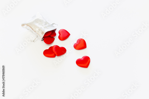 Close-up of a small shiny silver bag filled with cute red velvet hearts on white background. Concept of a romantic love gift for couples, valentines day, marriages or birthdays.