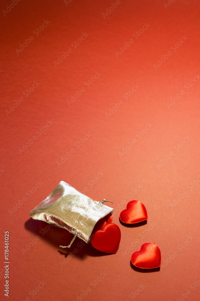 Close-up of a small shiny silver bag filled with cute red velvet hearts on red background. Concept of a romantic love gift for couples, valentines day, marriages or birthdays. Close-up of a small shiny silver bag filled with cute red velvet hearts on red background. Concept of a romantic love gift for couples, valentines day, marriages or birthdays.